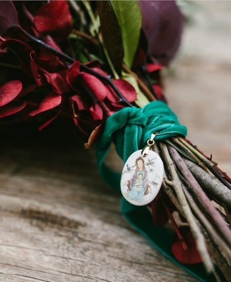 Medalla de cerámica con imagen mariana atada a ramo de flores rojas con cinta verde