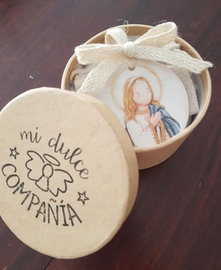 Medalla religiosa en caja redonda kraft con imagen angelical, presentada con lazo de cuerda