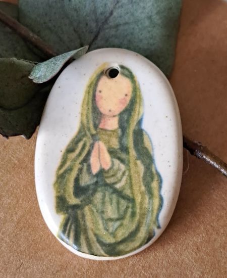 Medalla ovalada de cerámica con imagen de la Virgen María en tonos verdes, sobre fondo natural