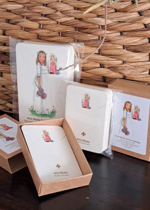 Recordatorios de Primera Comunión personalizados con ilustración de niña en vestido blanco y detalles religiosos, presentados en cajas de cartón.